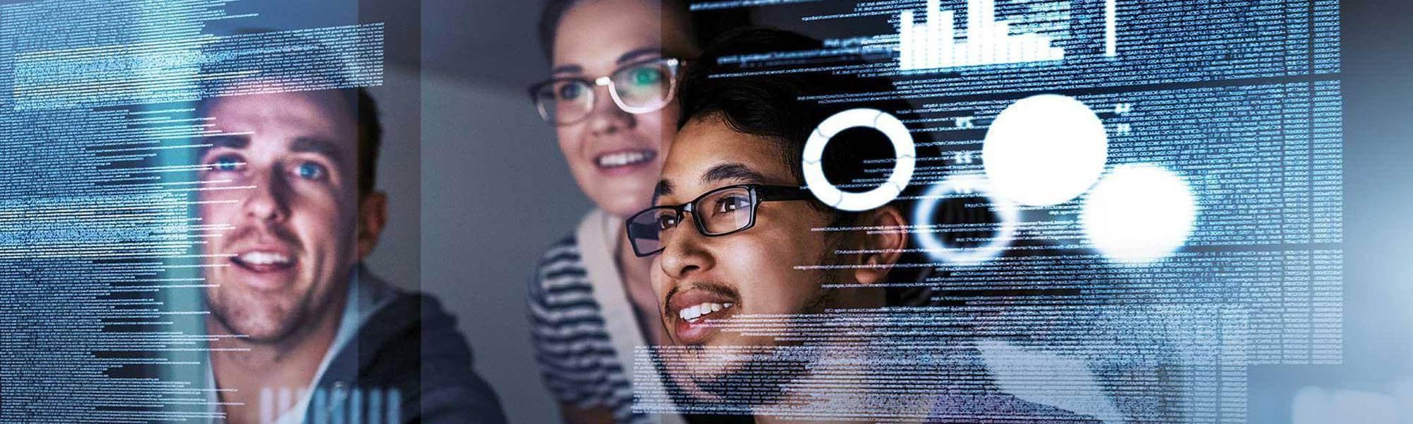 Photograph of the reflections of three students reviewing code on a computer monitor.